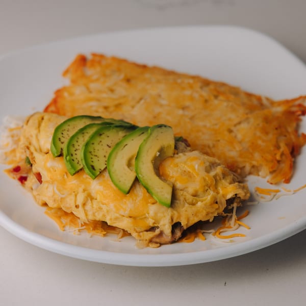Braxton's Kitchen omelet topped with avocado slices and shredded cheese, served with hash browns.