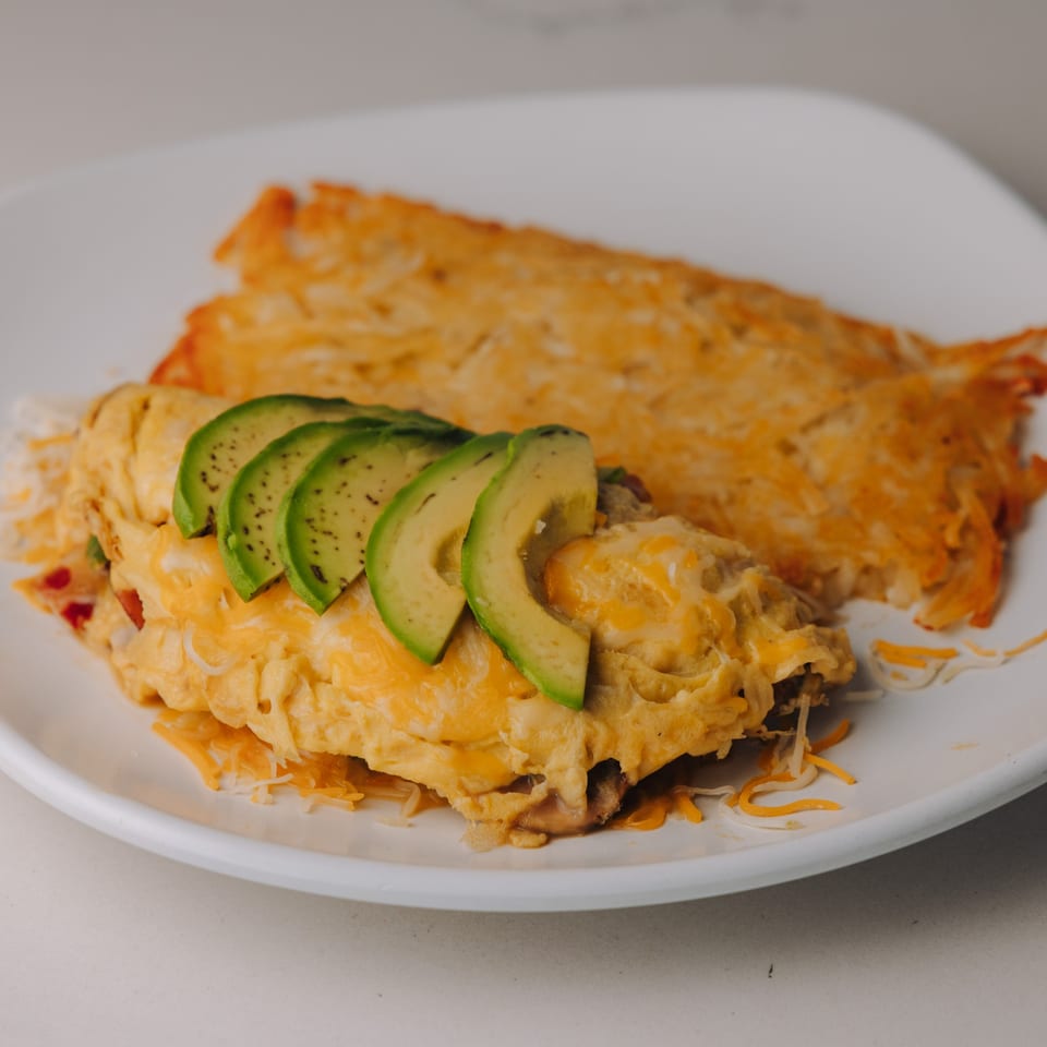 Braxton's Kitchen omelet topped with avocado slices and shredded cheese, served with hash browns.