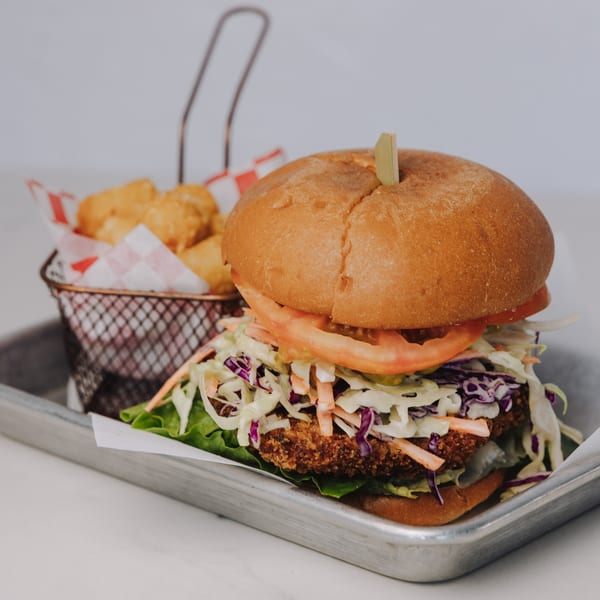 Braxton's Kitchen's fried chicken sandwich with coleslaw, tomato, and lettuce, served with tater tots.