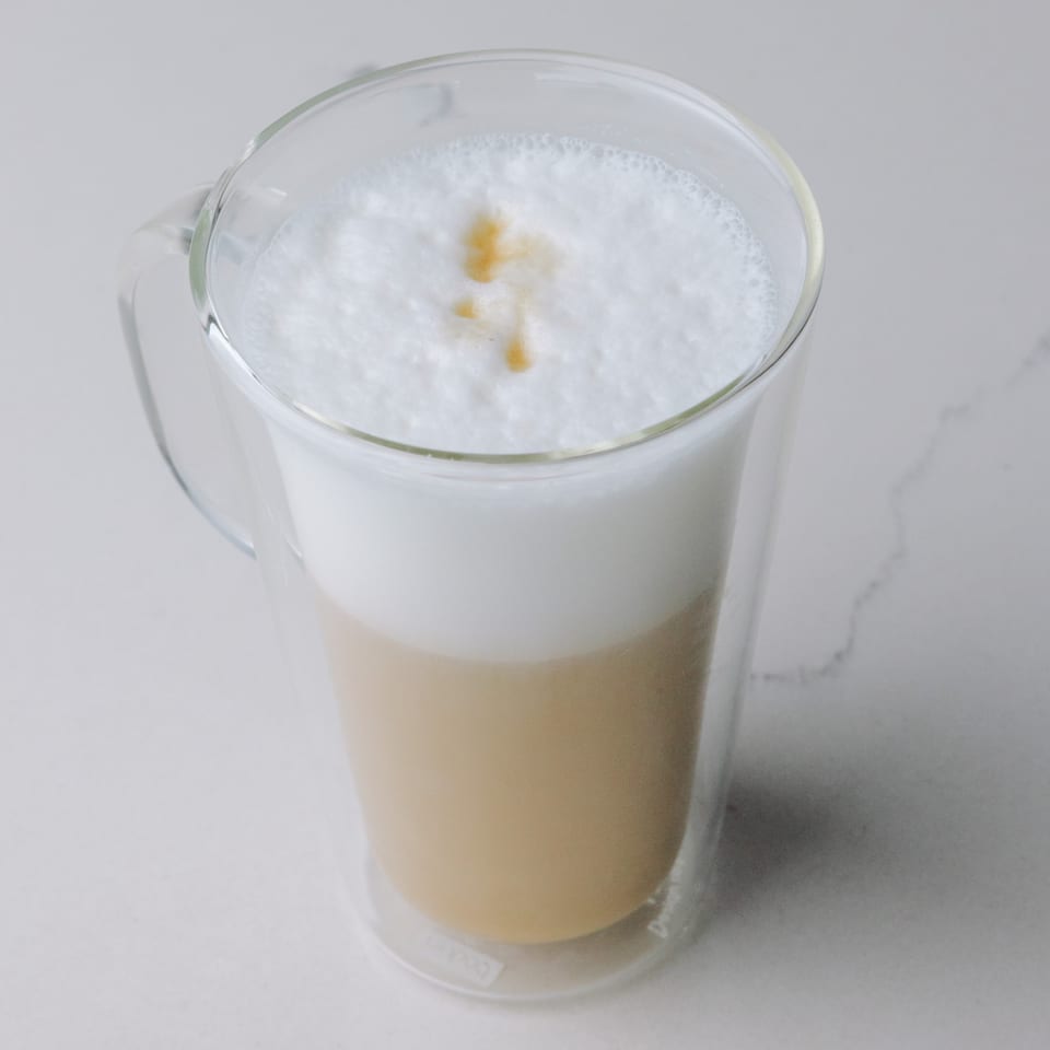Braxton's Kitchen latte in a clear mug with frothy milk and a drizzle of caramel.