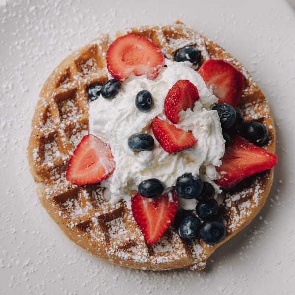 Braxton's Kitchen waffle topped with whipped cream, fresh strawberries, blueberries, and powdered sugar.
