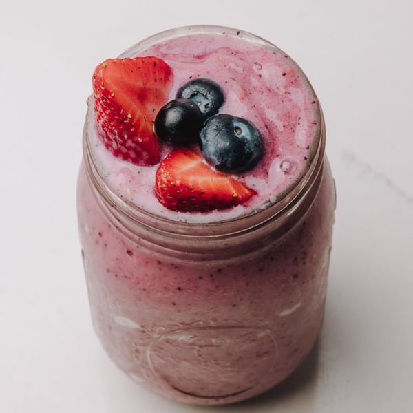 Braxton's Kitchen berry smoothie in a mason jar, topped with fresh strawberries and blueberries.