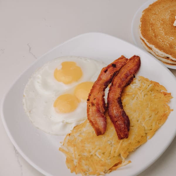 Braxton's Kitchen breakfast plate with fried eggs, crispy bacon, hash browns, and pancakes.