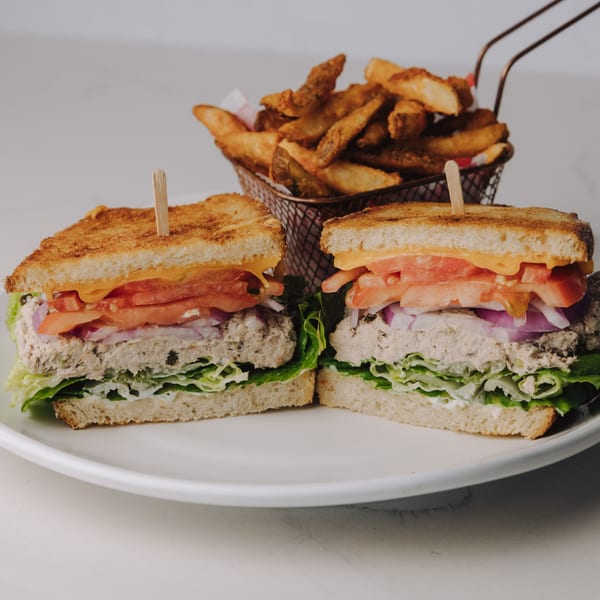 A tuna melt sandwich with lettuce, tomato, onion, and cheese, served with a side of potato wedges.